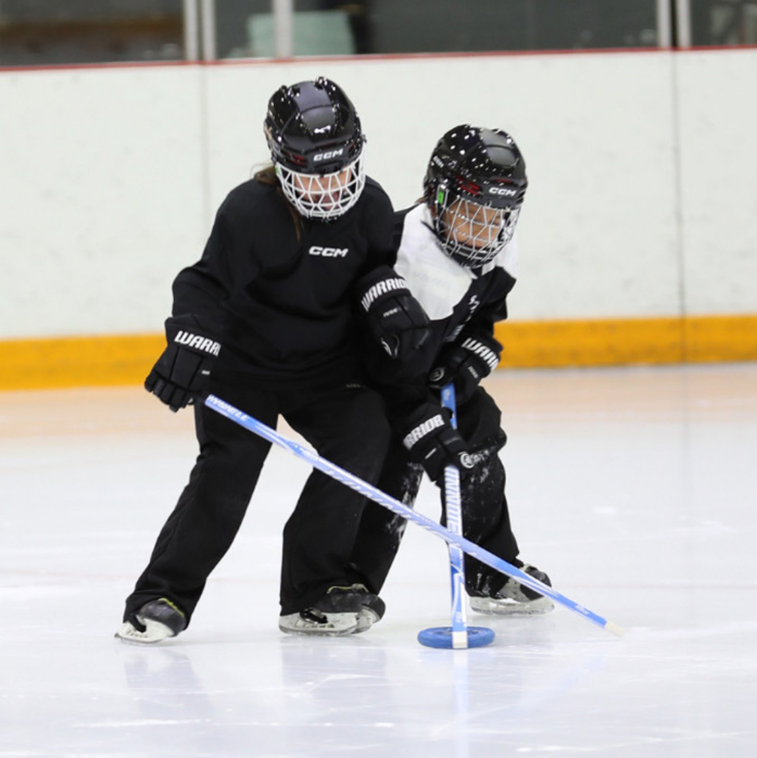 Two young kids play ringette on the ice together
